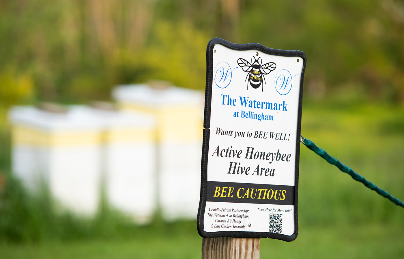 A bee hive sign in front of bee boxes.