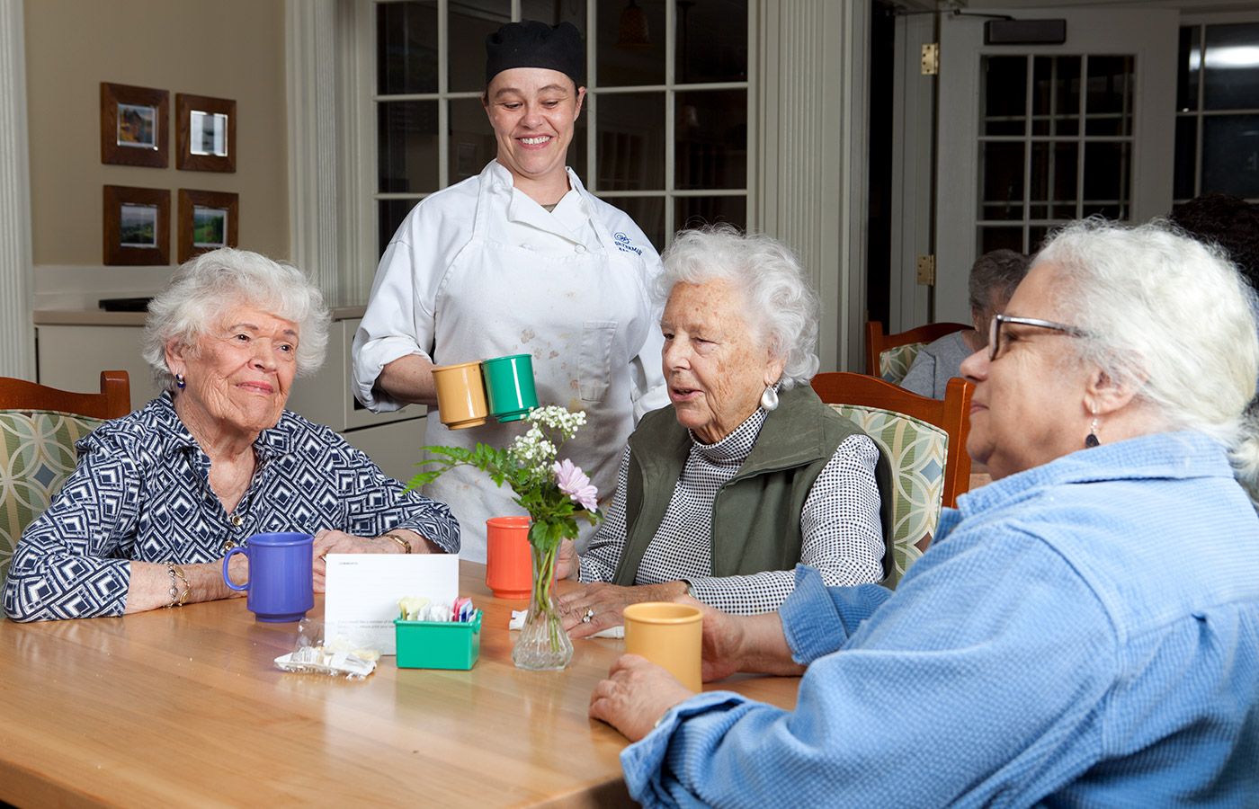 three residents sitting at table with a chef placing mugs down