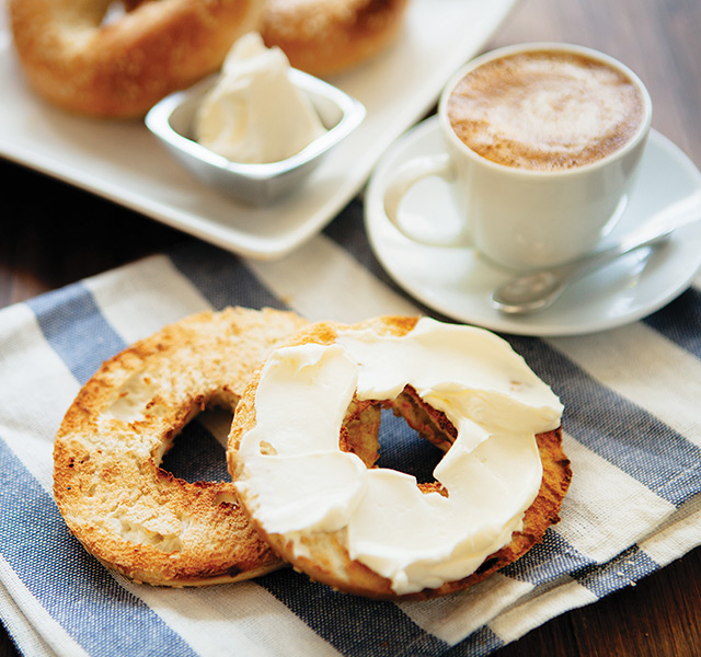 A cappuccino and bagel with cream cheese on a plate.