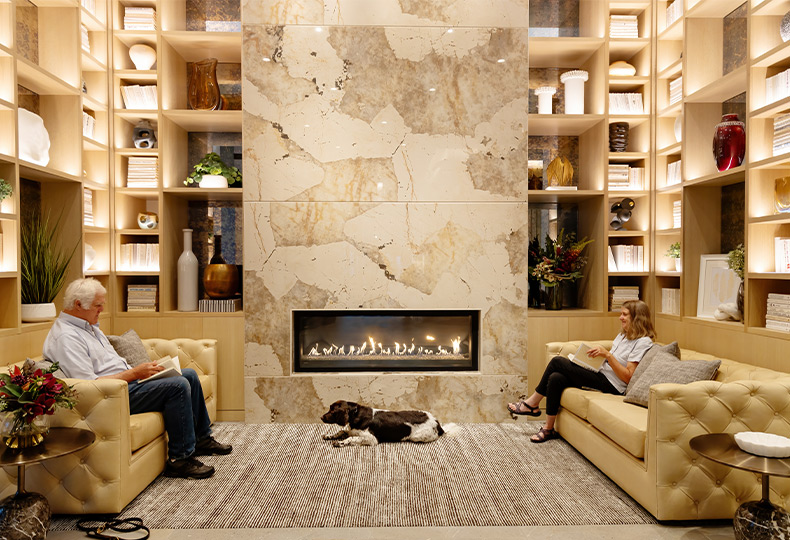 Two people sitting by the fireplace with a dog laying on the rug.