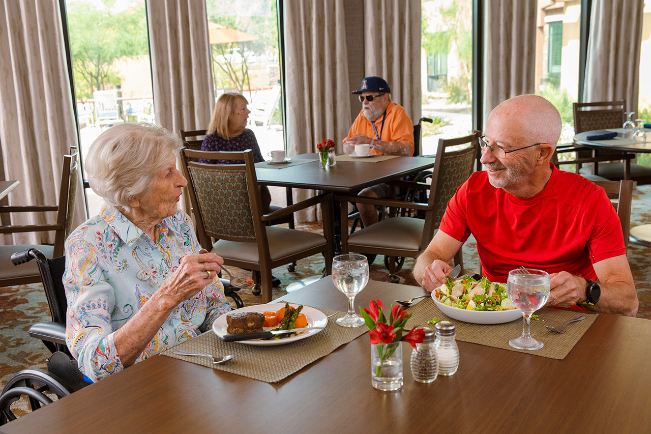 Two residents are sitting at a dining table enjoying a meal together.