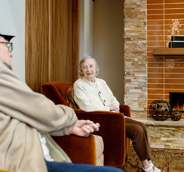 Two people sitting in chairs by a fireplace.
