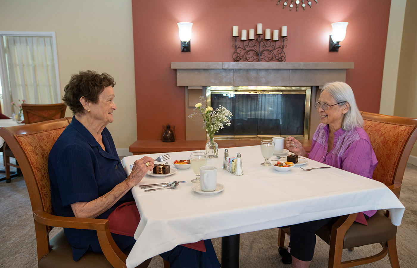 two women enjoying pastries sitting at dining table in front of fire place 