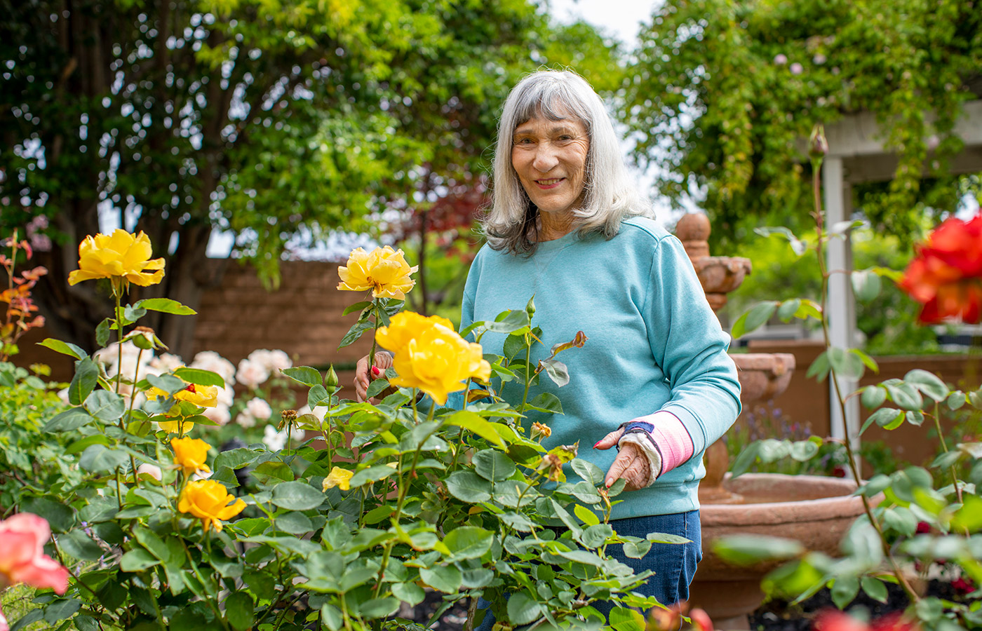 elderly woman smiling and standing by yellow flowers 