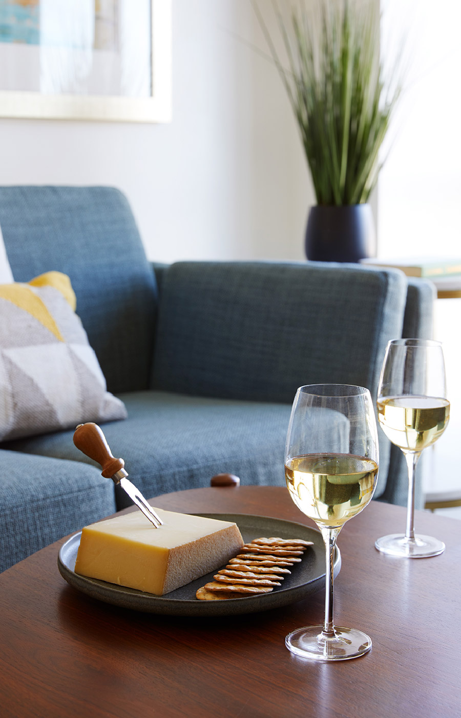 close up of cheese, crackers and wine on coffee table in front of sofa
