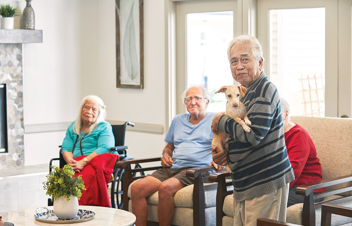 one resident is standing and holding a small dog in front of three seated residents