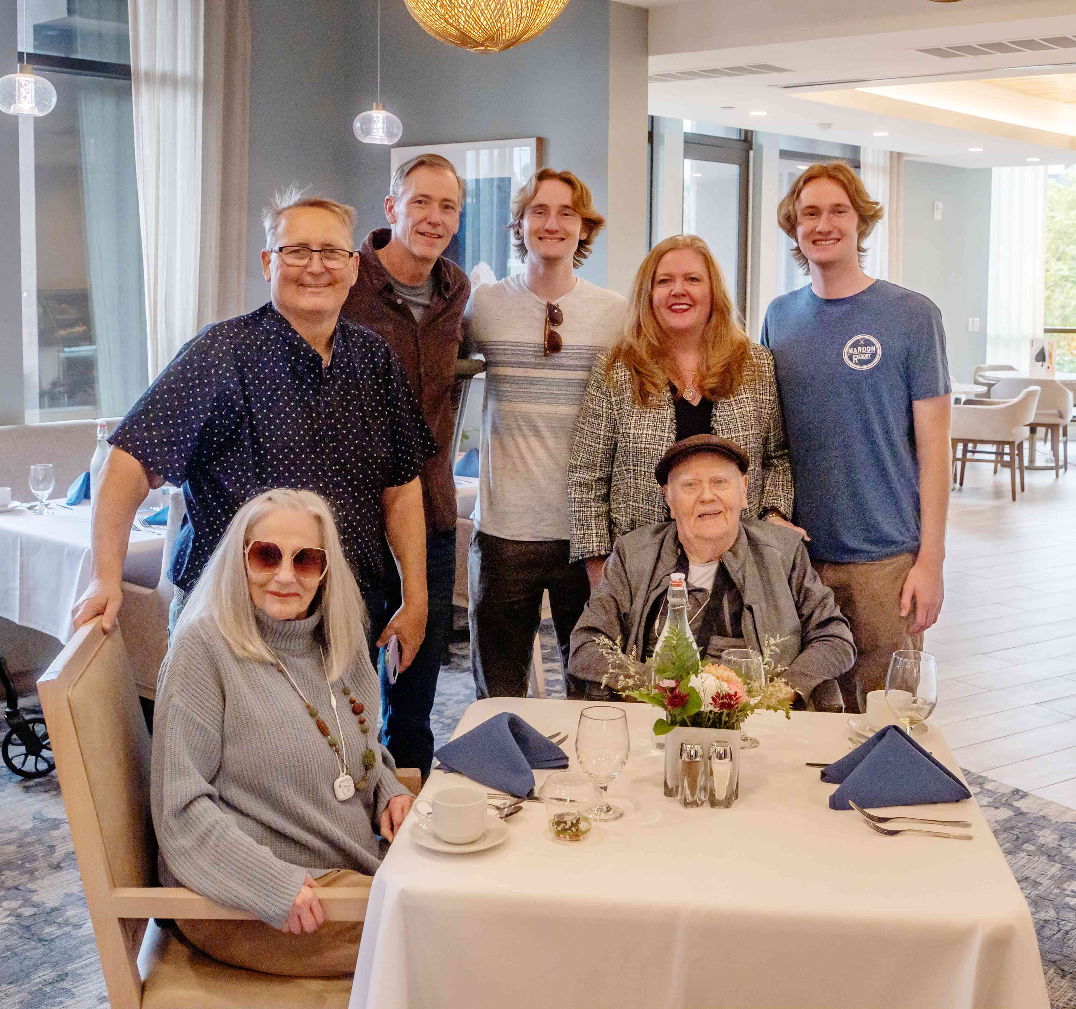 A family gathers around a resident in the dining room, sharing a warm moment across generations in a bright, welcoming setting.