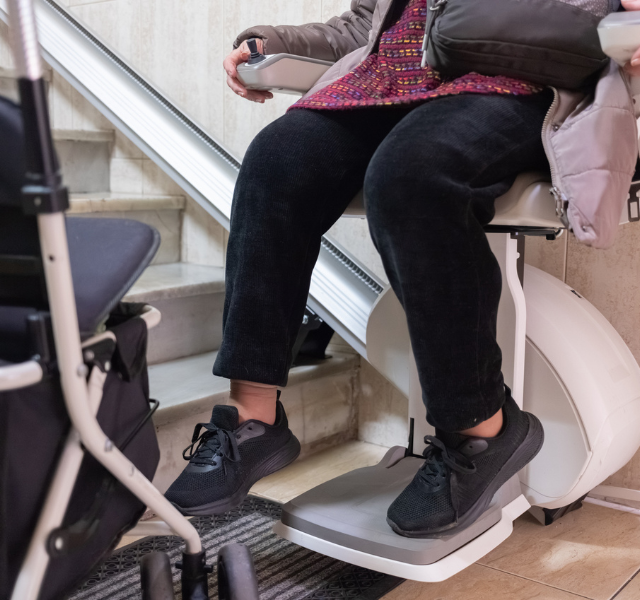 An older adult uses a stair lift at home, highlighting one of the adaptations families may make to support safety and mobility.
