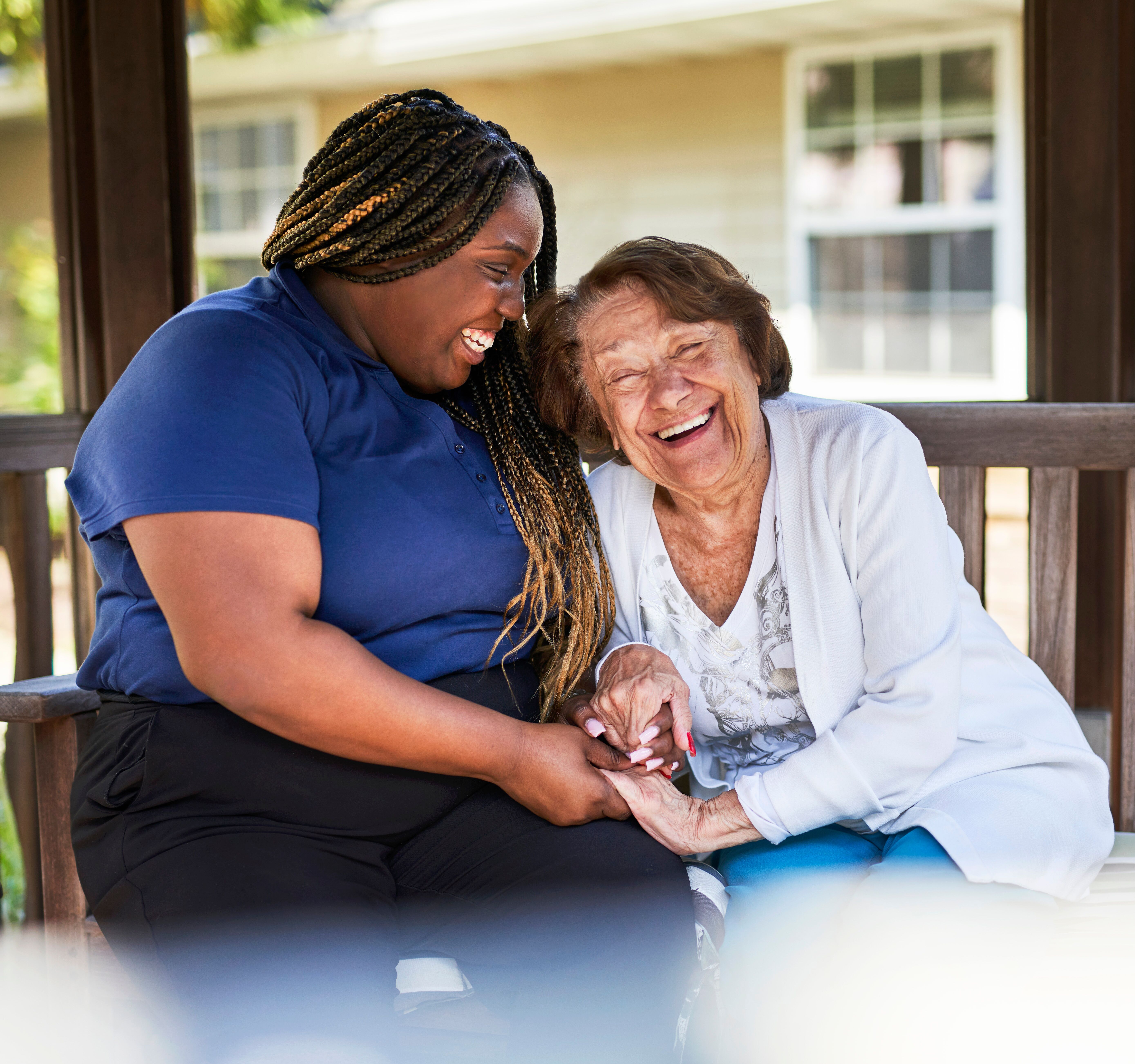 A resident and associate sit close together outdoors, laughing and holding hands during a warm, joyful moment.