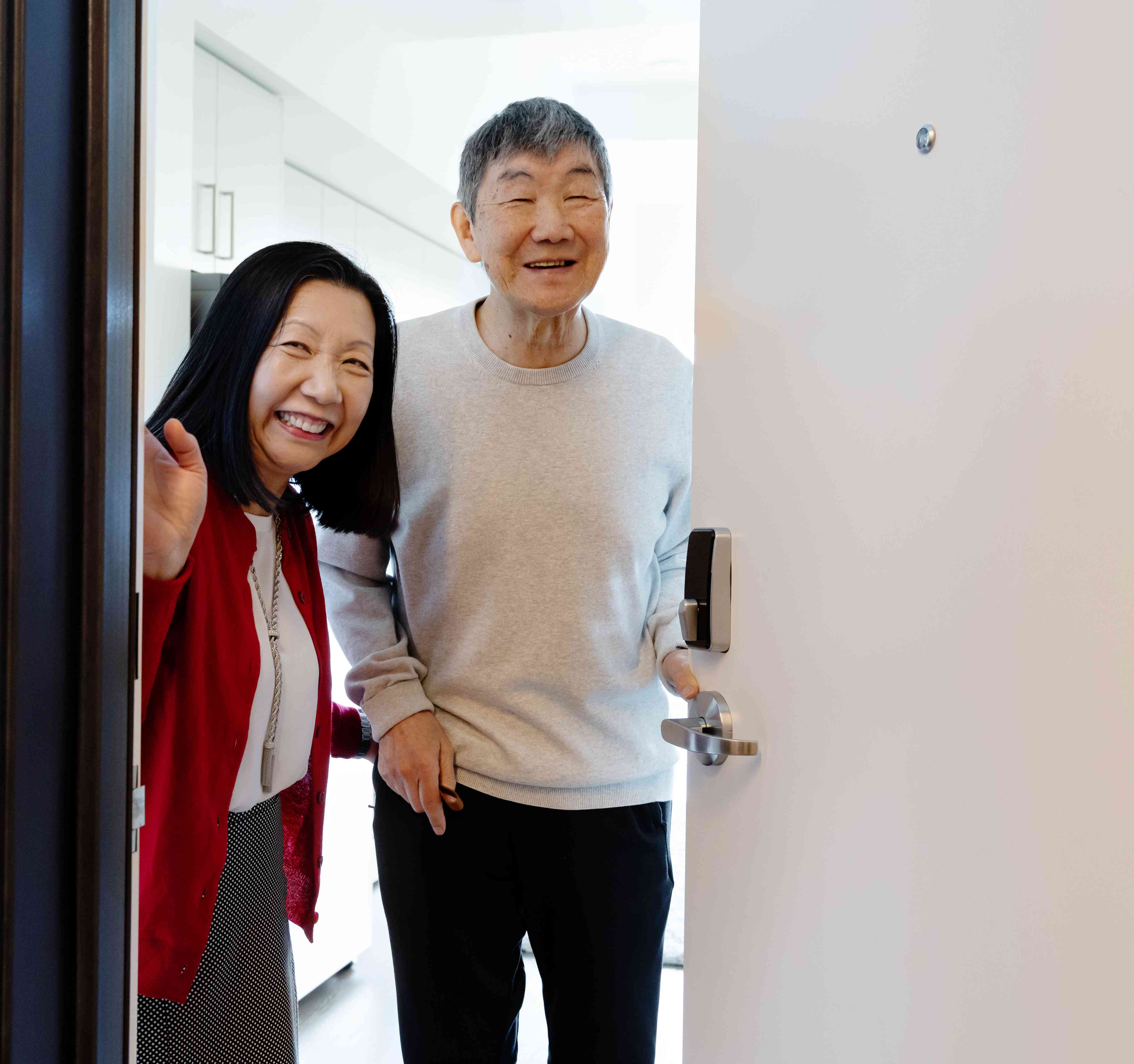 Two residents smile from the doorway of a bright apartment, offering a warm sense of welcome and home.