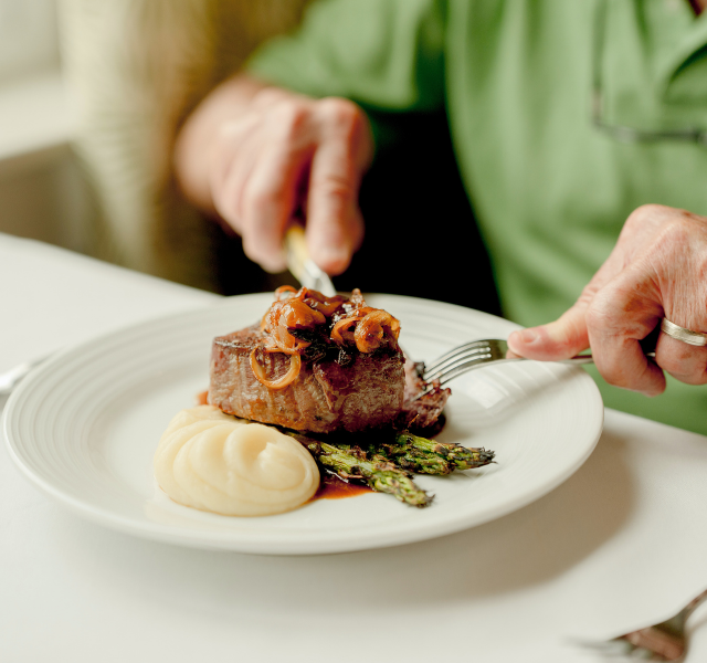 Close-up of steak and potatoes with someone in green shirt cutting into the steak.