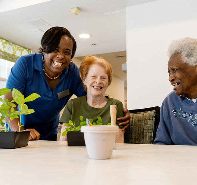 A caregiver with two residents and some plants on the table.