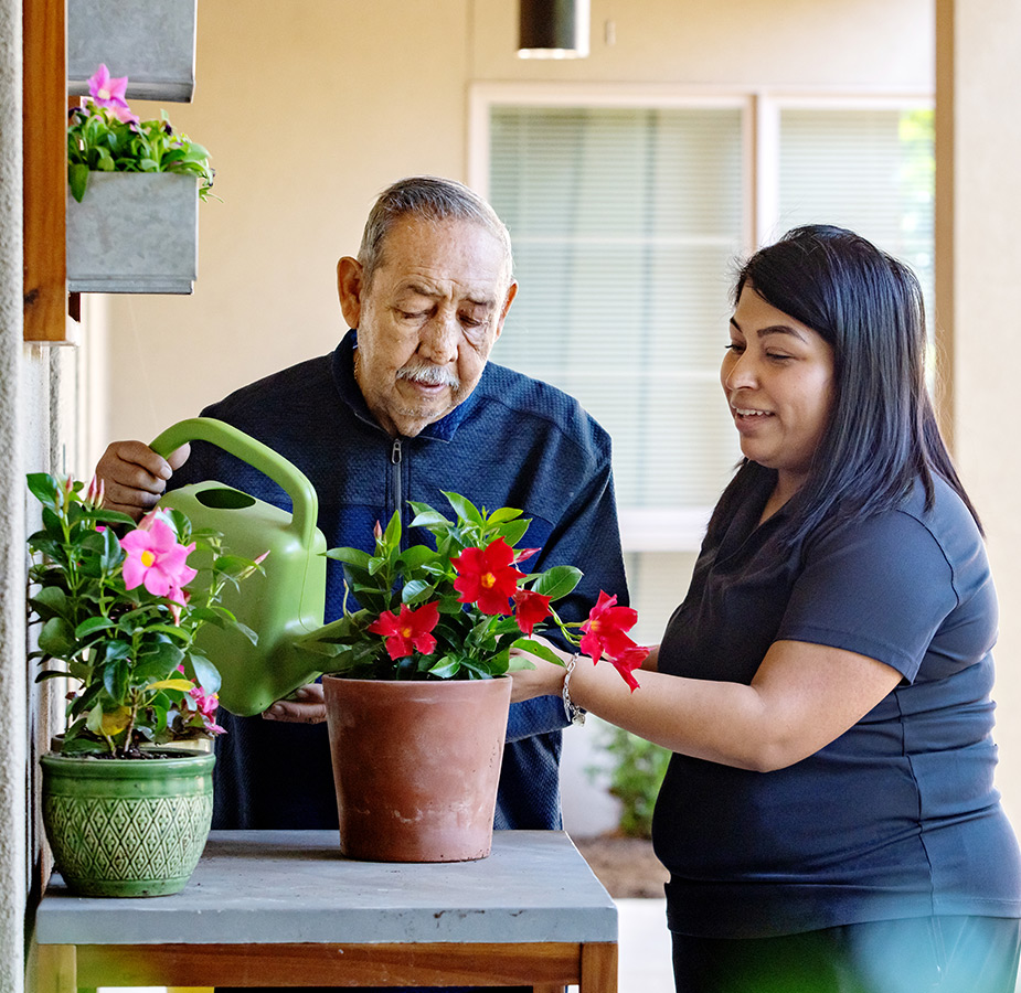 A caregiver helping a resident water plants.