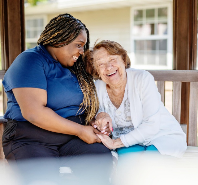 An associate and resident laughing and sitting on a bench outside in the summer.