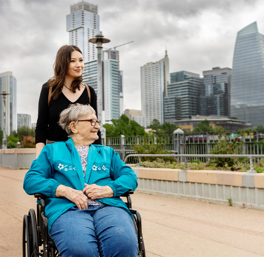 A person in a wheelchair with another in the city.