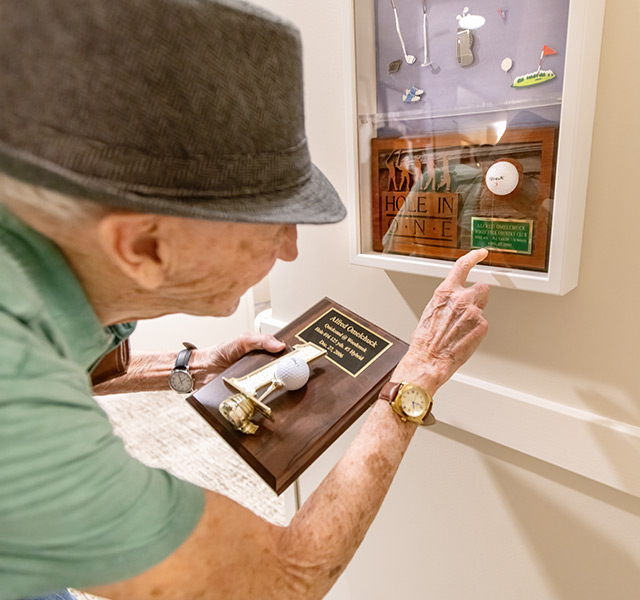 A resident pointing to the Hole in One award in their entry shadow box.