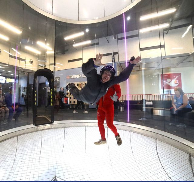 Indoor sky diving. Resident flying while instructor is standing next to them.