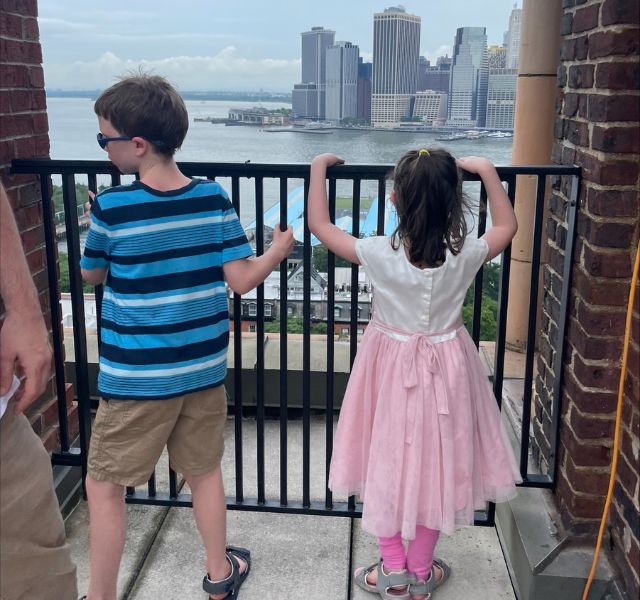 Two children on a roof top looking across the water to Manhattan.