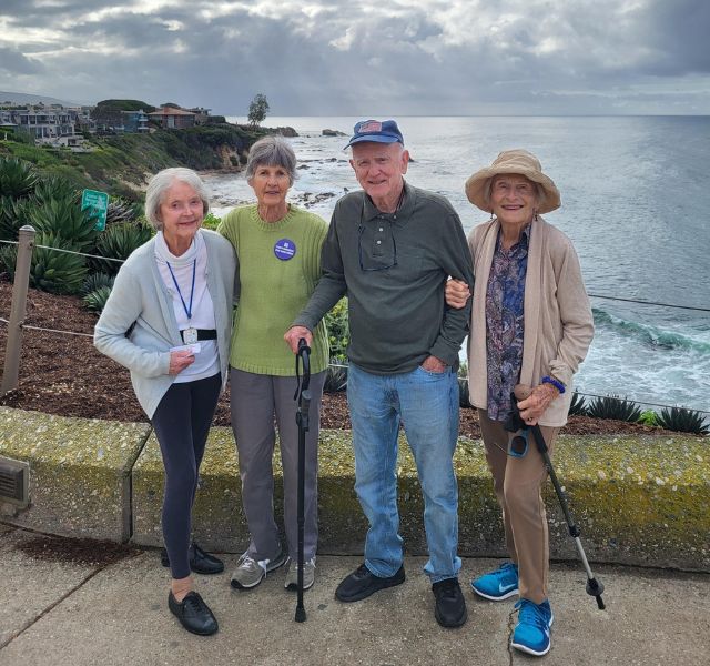 Four residents in tennis shoes and walking poles, standing on lookout over the ocean.