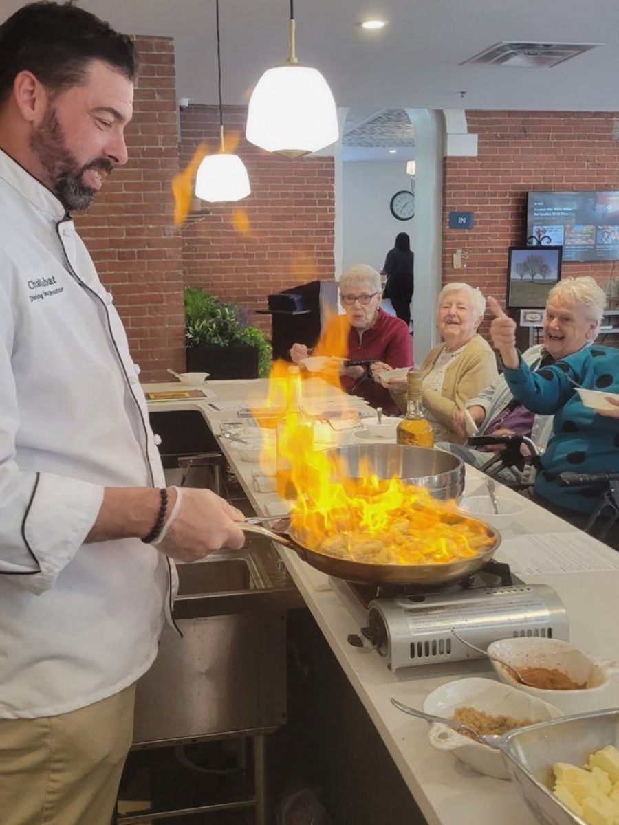 Chad, a chef, is flambéing food in front of residents.