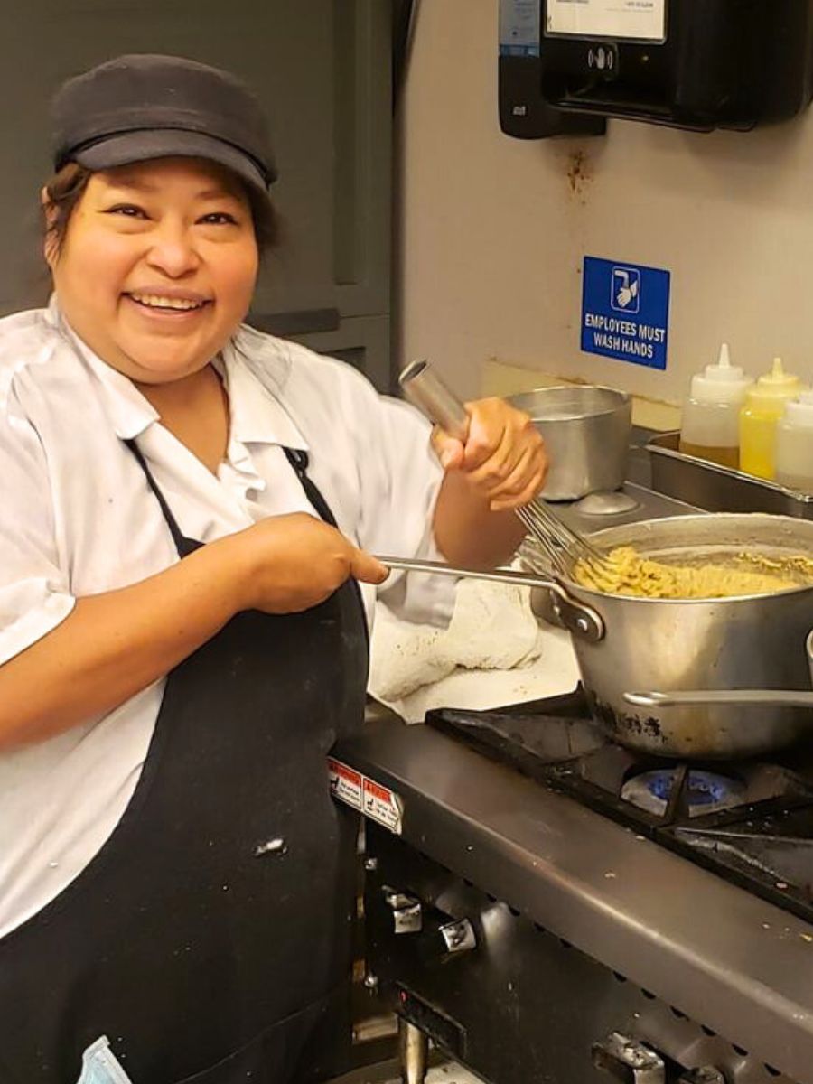 Reyna, a chef, is in the kitchen smiling and cooking.