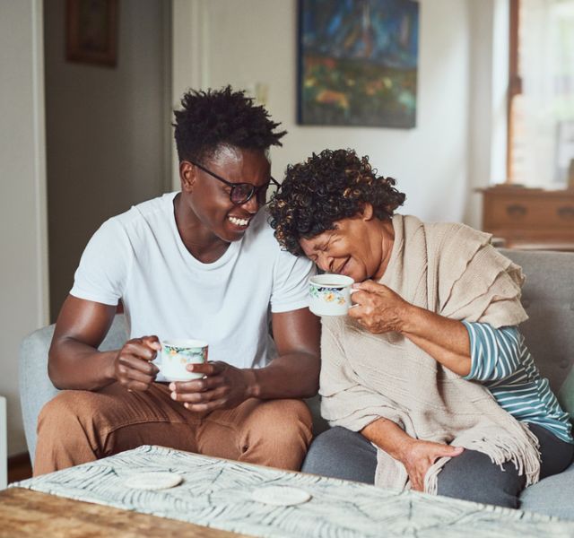Two people sitting on a couch with coffee, smiling.
