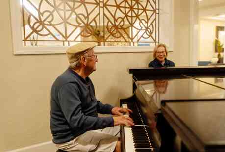 Member playing piano in the lounge and another member sitting nearby and smiling.