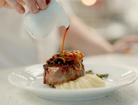 Chef pouring gravy on a steak.