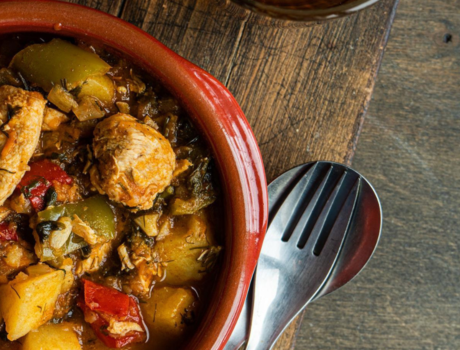 Chicken Curry in orange bowl. Spoon and fork rest on wooden table next to it.