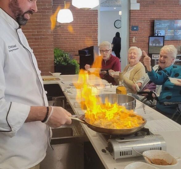 Chad, a chef, is flambéing food in front of residents.