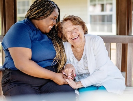 An associate and resident laughing and sitting on a bench outside in the summer.