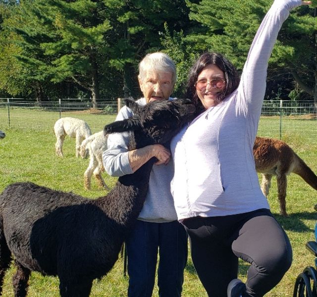 Resident and associate smiling with alpaca.