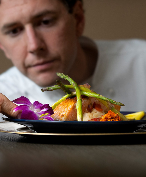 A chef placing a flower on a plate. A chef placing a flower on a plate.