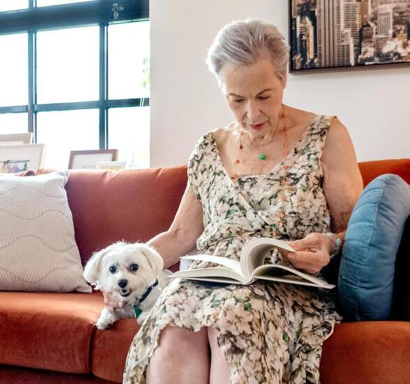 A resident on an orange couch sitting next to small white dog.