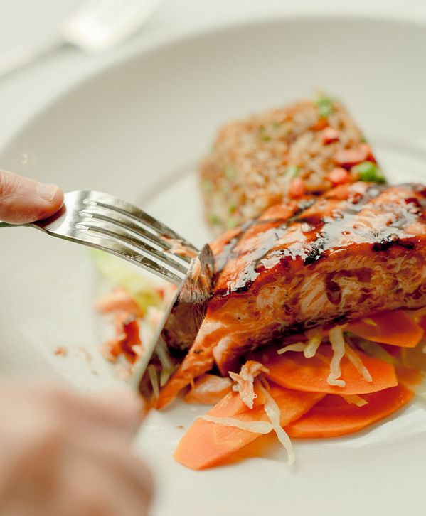 Accordion image A person cutting salmon on a plate.