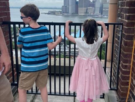 Two children on a roof top looking across the water to Manhattan.