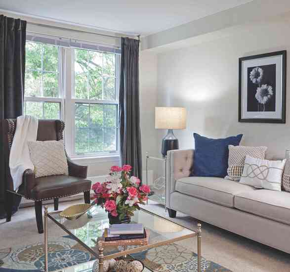 A light-filled apartment living room featuring large windows, soft neutral furnishings, and elegant decorative touches.