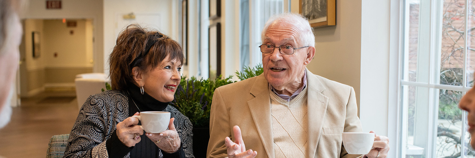 Two residents are having coffee with other residents.
