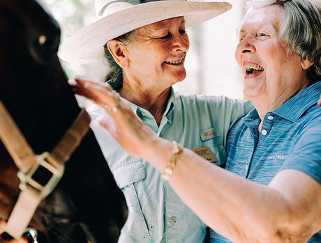 An associate and a resident laughing and petting a black horse.