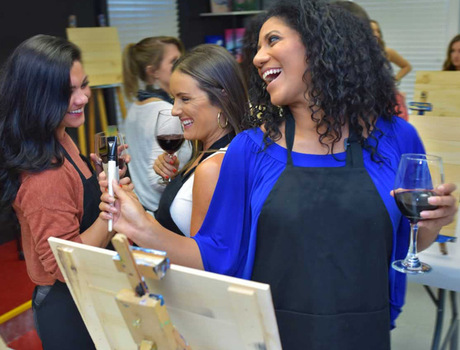 A few people laughing and enjoying wine during a paint class.