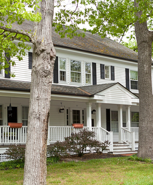 Accordion image A large white house with a wrap around porch.