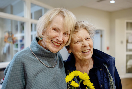 Two residents of the Fountains at Milbrook senior living community in Milbrook, NY, smiling and holding flowers.