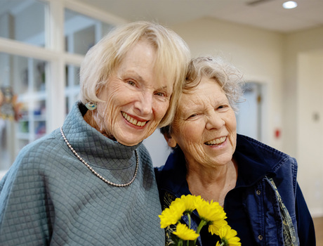 Two residents of the Fountains at Milbrook senior living community in Milbrook, NY, smiling and holding flowers.