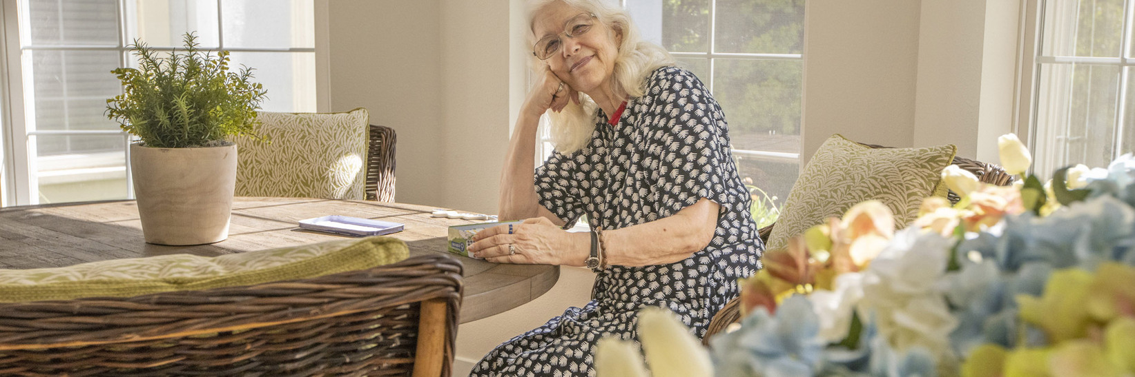 A resident sitting at a table near a large bouquet of flowers. A resident sitting at a table near a large bouquet of flowers.