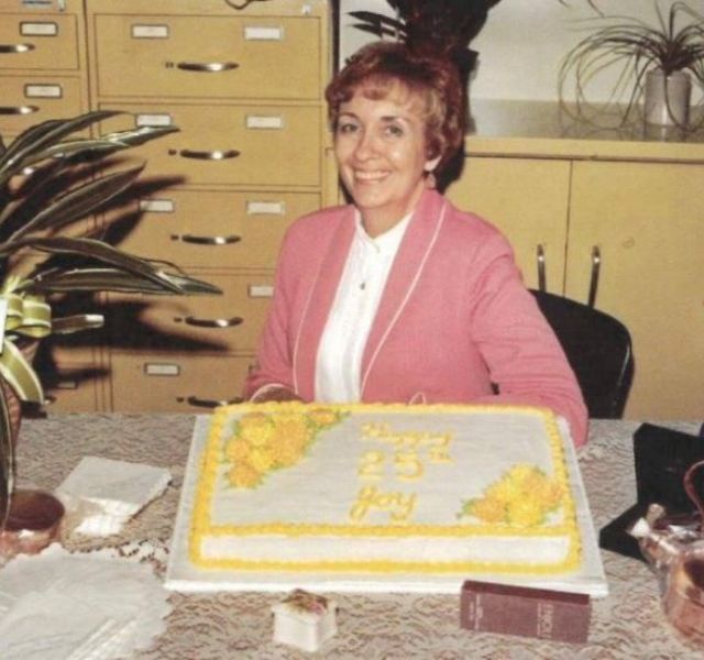 Woman sitting at desk with birthday cake in front of her.