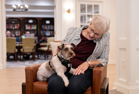 A person sitting in a chair with their dog at Watermark Laguna Niguel Senior Living Community .