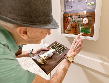 A resident pointing to the Hole in One award in their entry shadow box.