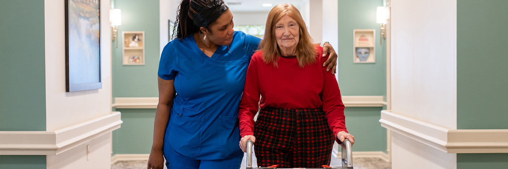 A personal care caregiver at Blue Bell Place assisting a resident in the hallway.