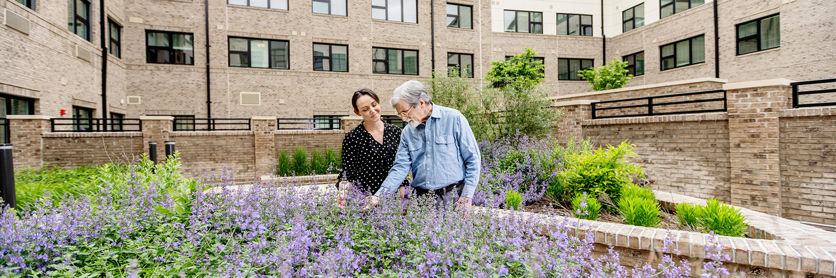 A naya caregiver walking through the courtyard with a memory care resident of The Sky Bridge at Town Center in Upper Marlboro, MD. A naya caregiver walking through the courtyard with a memory care resident of The Sky Bridge at Town Center in Upper Marlboro, MD.
