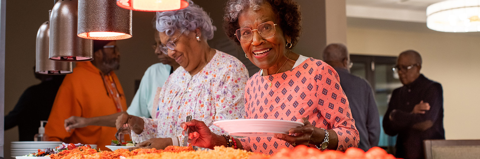 A group of people getting food from a buffet. A group of people getting food from a buffet.